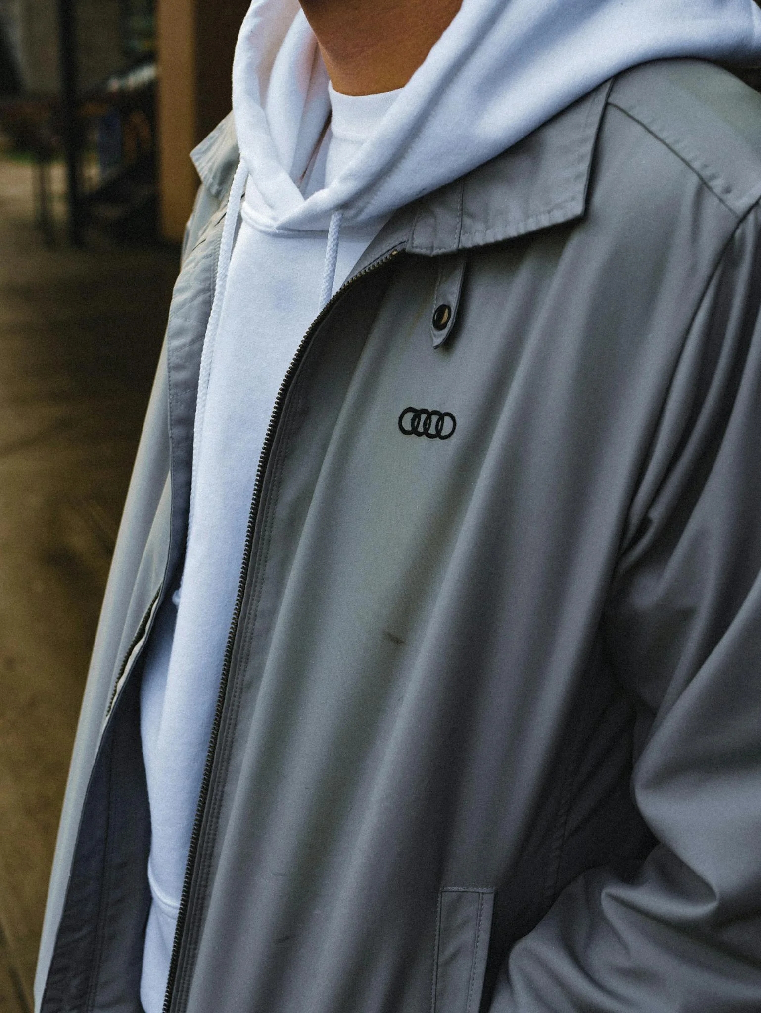 A man wearing a gray jacket and white hoodie standing outdoors, showcasing urban fashion.