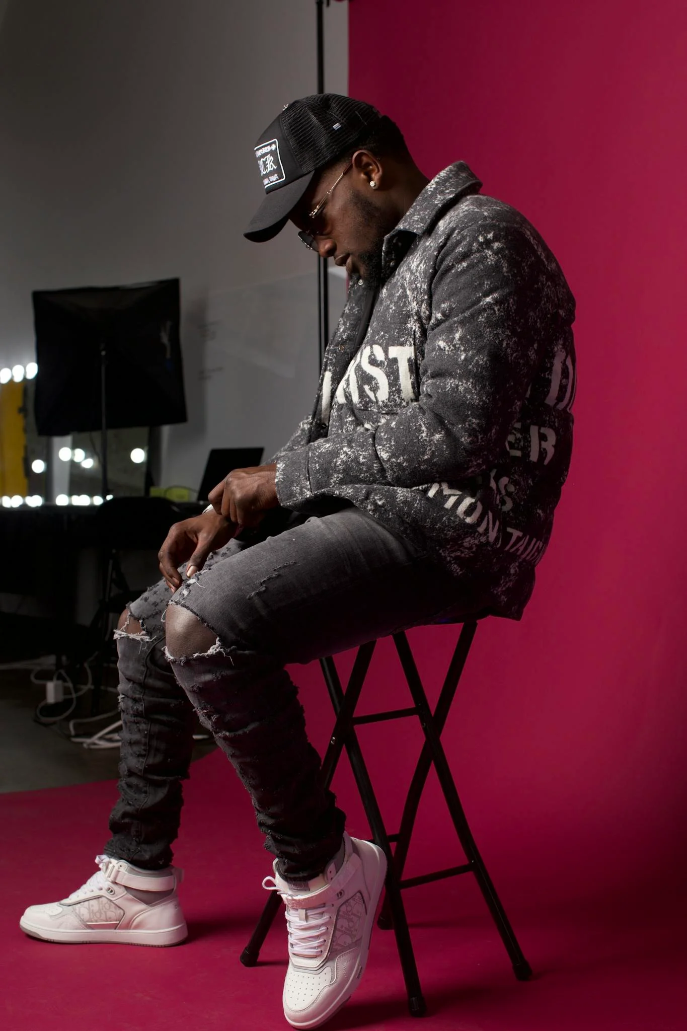 Stylish man in trendy attire sits against a red backdrop, showcasing urban fashion.